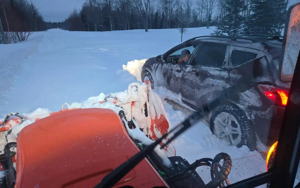 Damaged gray SUV stuck in deep snow on a winter road with red snowplow equipment in foreground