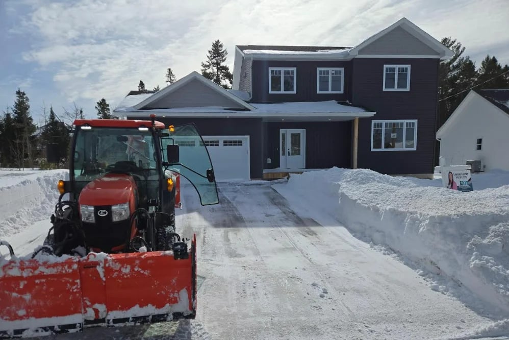 Red snow plow truck clearing a driveway in front of a dark two-story house in winter
